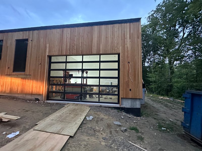 Contemporary full-view glass garage door on cedar building at dusk with interior lit
